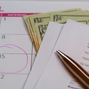 Calendar with words Tax Day , dollars and form 1040 income tax form showing tax day for April